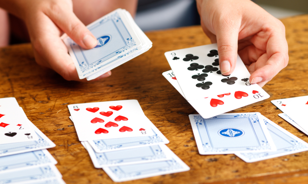 ndividual intently playing solitaire on a wooden coffee table with a spread of cards.
